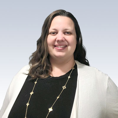 hearing care professional with long wavy hair, wearing a black top, a white cardigan, and a gold necklace