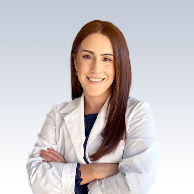 audiologist wearing a white coat with arms crossed against a light gradient background