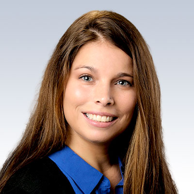 Hillary Masucci, a hearing care professional with long brown hair, wearing a blue collared shirt under a dark sweater.