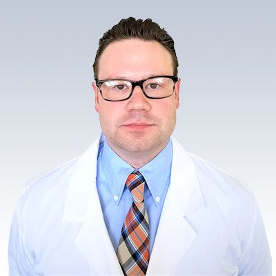 Hearing specialist wearing a white coat and a plaid tie against a gradient background.