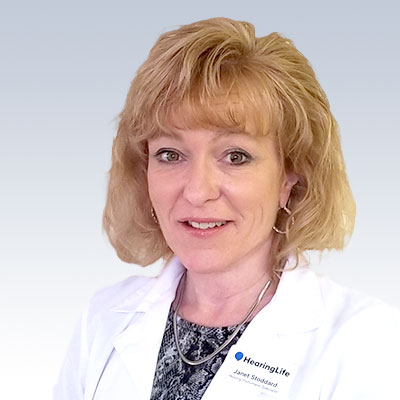 Janet Stoddard wearing a white lab coat with a HearingLife name badge.