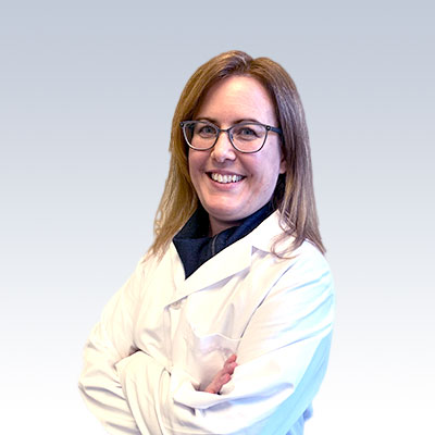 Hearing care specialist in a white lab coat crossing arms against a gradient background.