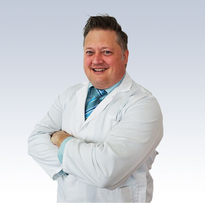 Jonathan Barcus, hearing care specialist wearing a white lab coat and blue tie, arms crossed.