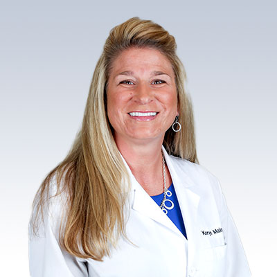 Keryn Maionchi wearing a white lab coat with long blonde hair against a light gradient background.