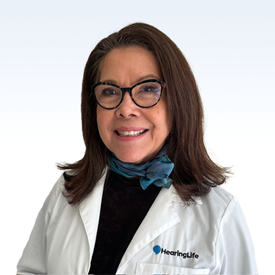 Mary San Miguel, hearing care professional at HearingLife, wearing a white lab coat and blue scarf.