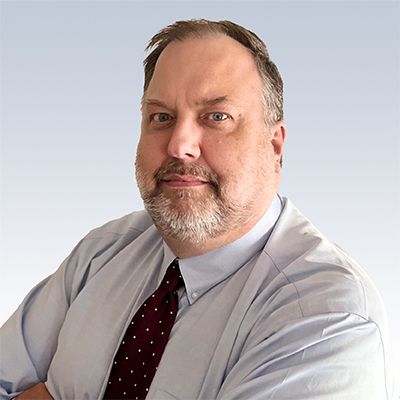 Mike Massie, hearing care professional wearing a light dress shirt and patterned tie, standing against a neutral background.