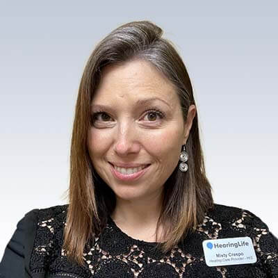 Misty Crespo, Hearing Care Provider at HearingLife, wearing a black lace top and a name badge against a neutral background.