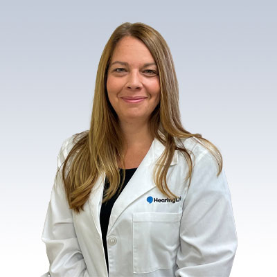 Nicole Munday wearing a white hearing care professional coat with a HearingLife logo.