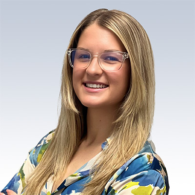 Paige Wendling, hearing care professional, wearing glasses and a colorful blouse against a light gradient background.