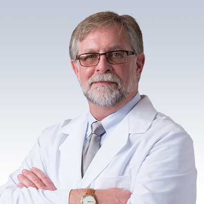 Paul Stephens wearing a white lab coat with arms crossed against a gradient background.