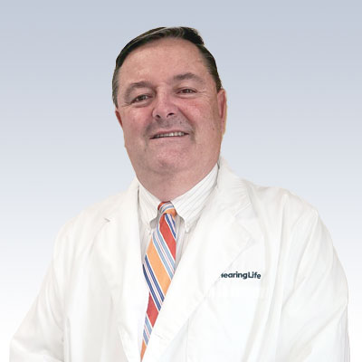 Rick Beare, hearing care professional at HearingLife, wearing a white lab coat with a colorful striped tie.