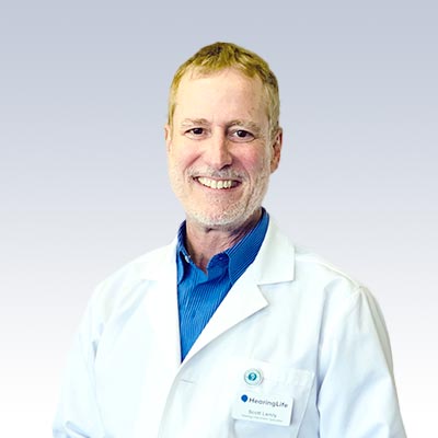 Scott Lemly wearing a HearingLife lab coat against a gradient background.