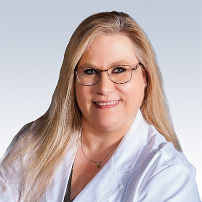 Shannon Foster, hearing care professional in a white coat with long blonde hair against a light blue background.