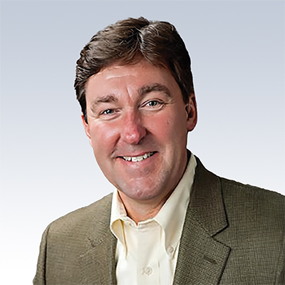 Stan Warner, hearing care specialist wearing a beige jacket and white shirt against a light gradient background.
