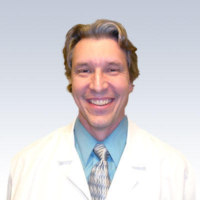 Steve Smith wearing a white lab coat, blue shirt, and patterned tie against a gradient background.