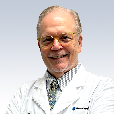 Thomas Humphries, hearing care specialist wearing a white coat with a tie, representing professional hearing health services.