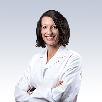 Hearing care professional wearing a white lab coat with arms crossed.