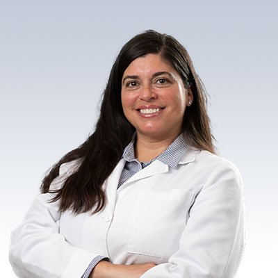 Toni Muradov wearing a white lab coat with arms crossed, standing against a gradient background.
