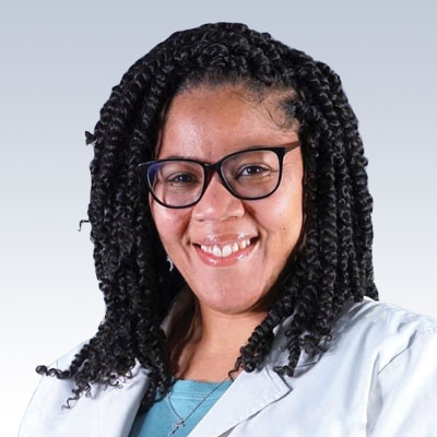 Hearing care professional with curly black hair wearing a lab coat and blue shirt.