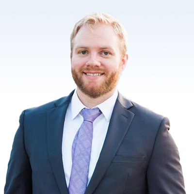 Ty Wagner wearing a suit and light purple tie against a light gradient background