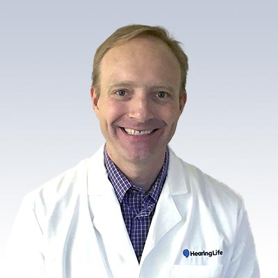 Aaron McElhinney wearing a white lab coat with a HearingLife logo.