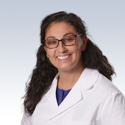 Alicia Huysmans wearing a white lab coat against a light gradient background.