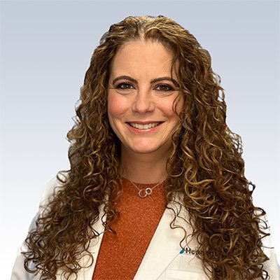 anne catapano, hearing care specialist wearing a white coat, with long curly hair and a neutral background