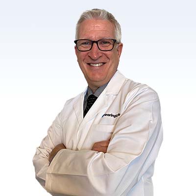 Hearing care professional wearing a white lab coat with arms crossed.