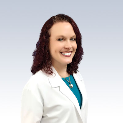 Christi Clark wearing a white lab coat against a light gradient background.
