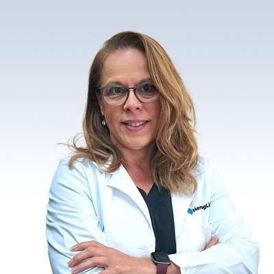 Christine Walters wearing a white medical coat with a hearing care clinic logo, standing against a light gray background.