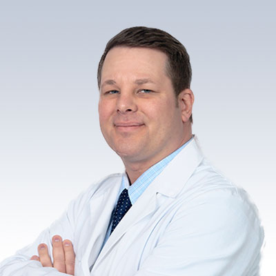 Craig Hand wearing a white lab coat with arms crossed against a light gradient background.