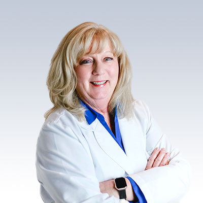 Donna Runkle, hearing care professional, wearing a white coat with arms crossed.