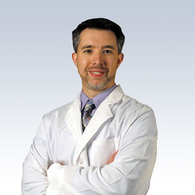 Erik Raml wearing a white lab coat with arms crossed against a gradient background.