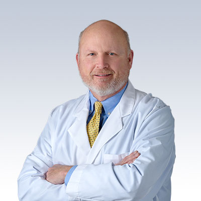 Gerald Hug wearing a white lab coat and yellow tie, representing a hearing care professional.