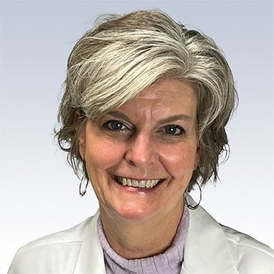 Hollie Bahen, hearing care professional with short gray hair wearing a white coat and purple top.