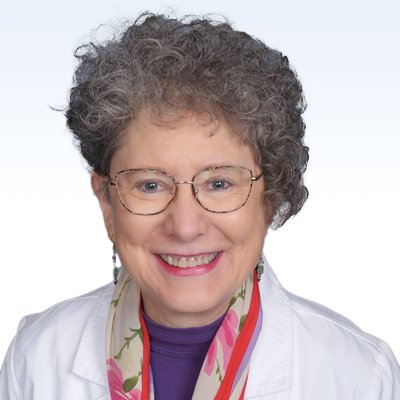 Hearing care professional with curly gray hair wearing a white coat and colorful scarf.