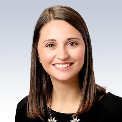 Katrina Smith, hearing care specialist, wearing a black top with a floral necklace, against a light gradient background.