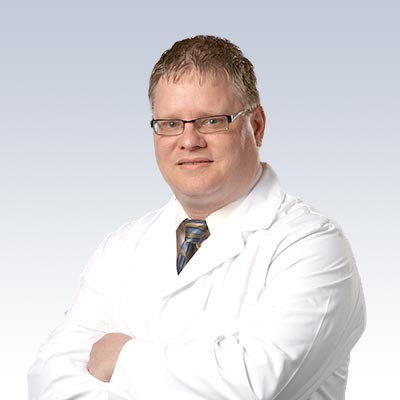 Ken Clark wearing a white lab coat with arms crossed, representing a professional in hearing care.