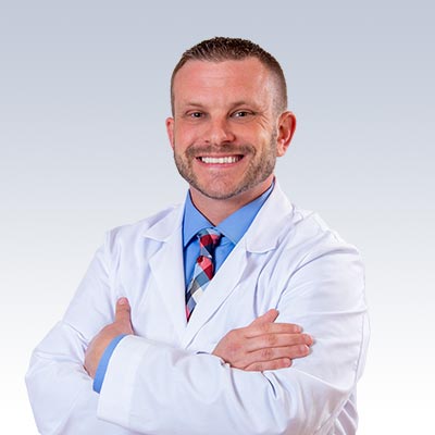 Korrey Shoup wearing a white lab coat and crossed arms against a light gradient background