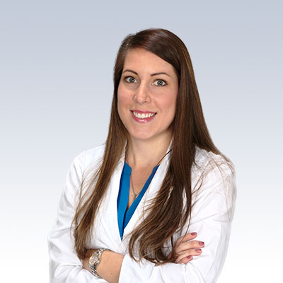 Lauren Fraley, hearing care professional, in a white coat with arms crossed against a gradient background.