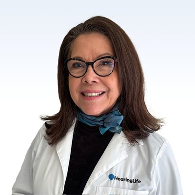 Mary San Miguel, hearing care professional at HearingLife, wearing a white lab coat and blue scarf.