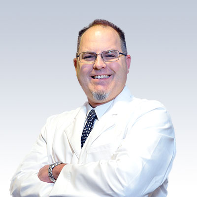 Paul Ebben wearing a white lab coat with arms crossed, showcasing professionalism in hearing care services.