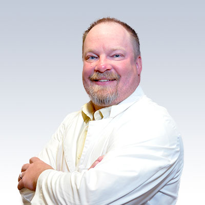 Rich Flunker wearing a white lab coat with arms crossed, representing a professional in hearing care.