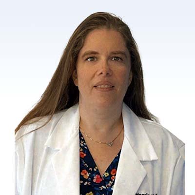 Ronni Mathews wearing a white lab coat with a floral blouse, representing a professional in hearing care services.