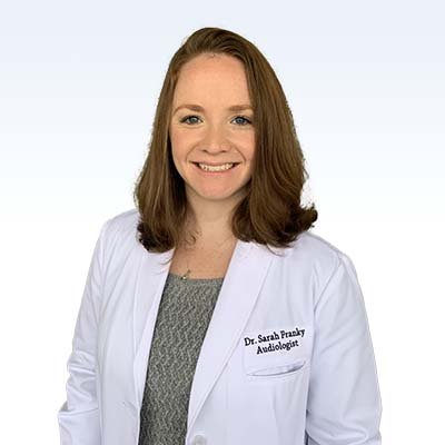 Dr. Sarah Franky, audiologist, wearing a white lab coat with her name badge visible.