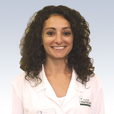 Hearing care professional in a Total Hearing Care lab coat with curly hair.