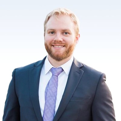 Ty Wagner wearing a suit and light purple tie against a light gradient background