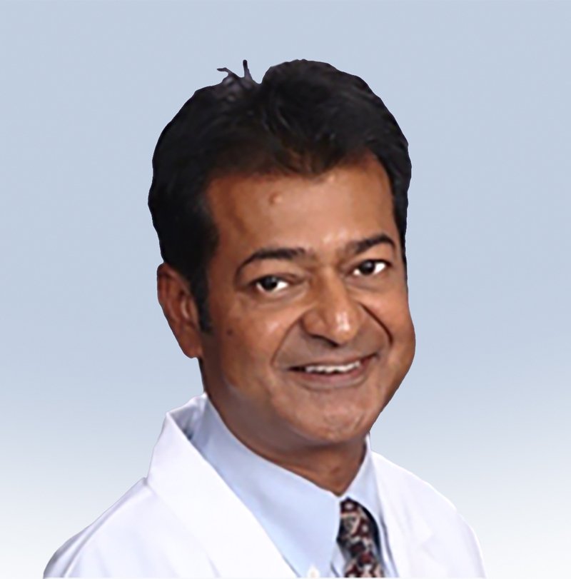 A man wearing a white medical coat and patterned tie smiles, with a light blue gradient background.
