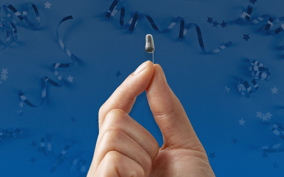You're Approved! Very small Oticon Own Hearing Aid being held by two fingers
