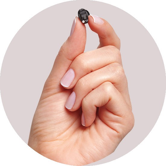 A hand with light pink nail polish holds a tiny black electronic device between the thumb and index finger, against a light gray background.